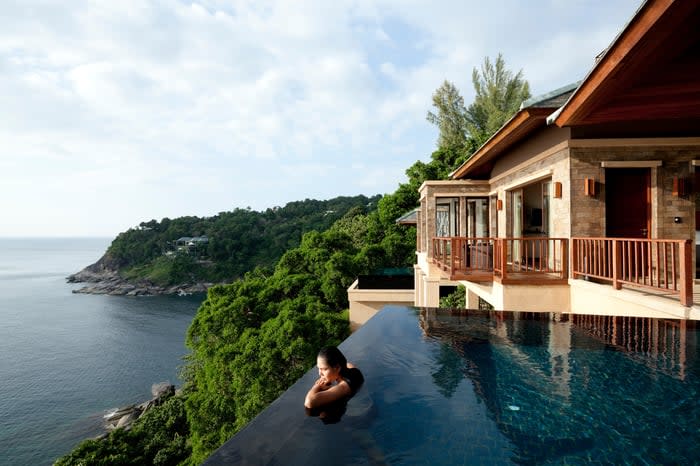 A person at the edge of an infinity pool on a cliff near the ocean.